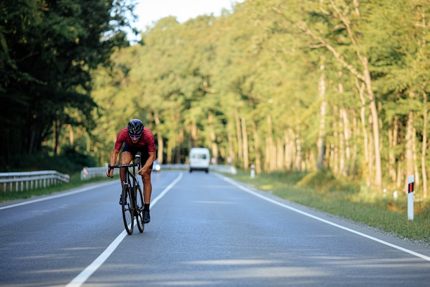 Homem ativo com corpo musculoso vestindo roupas esportivas andando de bicicleta no meio de uma estrada de asfalto