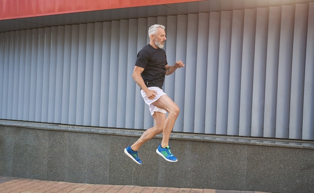 Homem ativo de meia-idade e esportivo em roupas esportivas, fazendo exercícios de salto enquanto se exercita