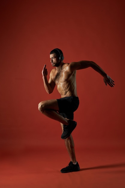Homem atleta focado em fones de ouvido fazendo exercícios de fitness isolados em fundo vermelho