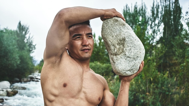 Homem atleta muscular cazaque treina e exercícios à beira do rio na natureza. Bonito asiático faz exercícios físicos extremos ao ar livre