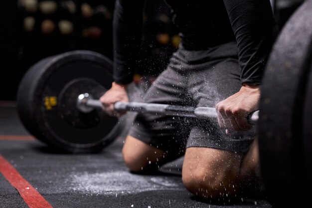 Homem atleta recortado está se preparando para o treinamento de cross fit. o levantador de peso cúmplice usa talco para levantar peso. em uma academia moderna, centro de fitness