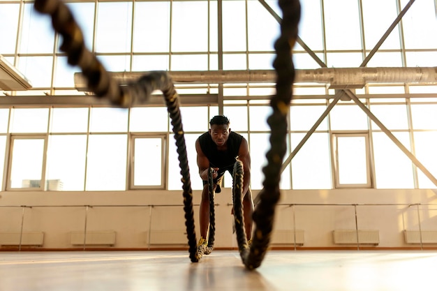 Homem atlético afro-americano em roupas esportivas treinando no ginásio e agitando as cordas