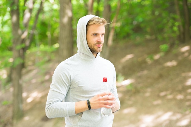 Homem atlético de tempo de descanso com garrafa de água Atleta bebe água após o treinamento em cuidados com o parque hidratação corporal esporte e homem de saúde no capô bebe água refrescante bebida vitamínica após treino