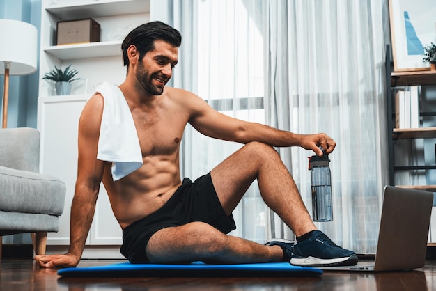 Homem atlético e desportivo descansando em um tapete de fitness durante uma sessão de exercícios corporais on-line para um físico apto e um estilo de vida desportivo saudável em casa Conceito de treinamento de exercícios em casa Gaiety