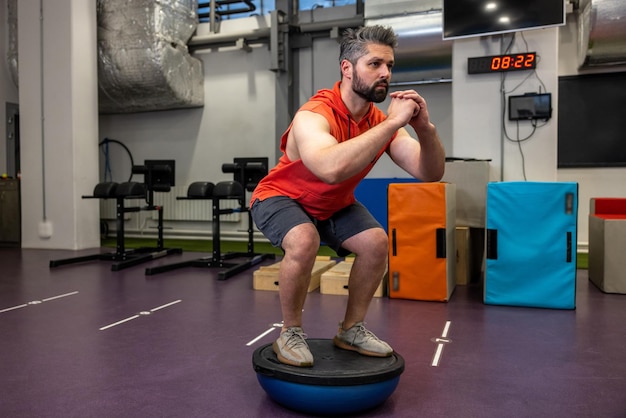 Homem atlético em forma realizando exercícios no hemisfério de ginástica bosu bola no ginásio fazendo abdominais