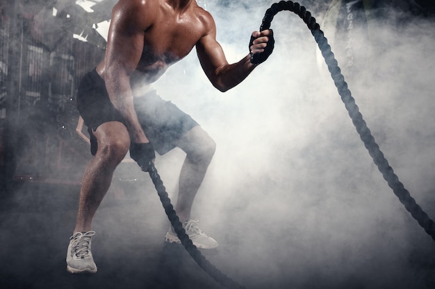 homem atlético fazendo exercícios de crossfit com corda em um ginásio enfumaçado