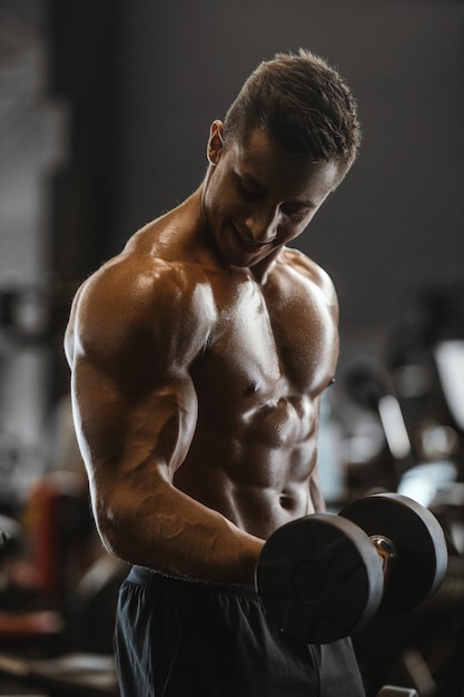 Foto homem atlético forte bonito, bombeando os músculos treino fitness e conceito de musculação fundo - homens de aptidão muscular fisiculturista fazendo braços abdominais, exercícios nas costas no tronco nu de ginásio