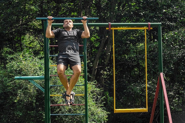 Homem atlético realiza exercícios de pull-up na barra horizontal na área externa infantil