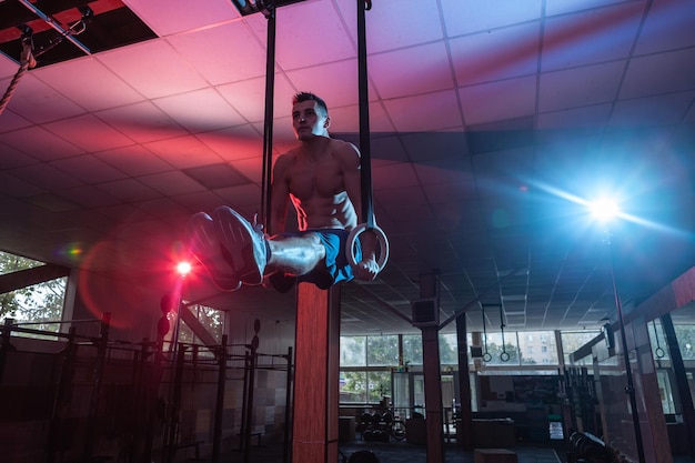 Homem atlético se exercitando em anéis de ginástica em luz de gradiente de néon azul vermelho