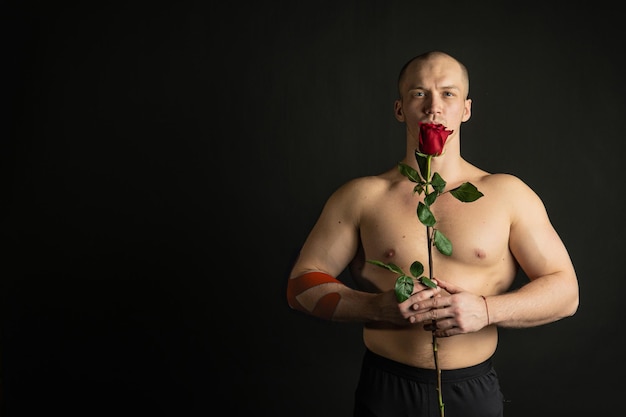 Homem atlético segurando uma rosa vermelha nua para o dia de velentin bombeou em seu braço um pingo de