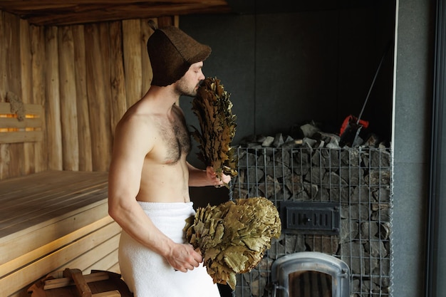 Homem atraente cheirando uma vassoura na sauna