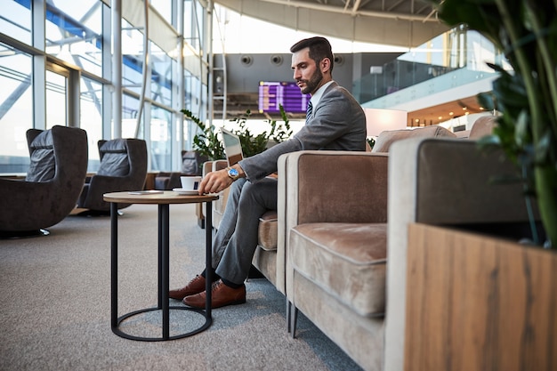 Homem atraente com café e gadget no saguão do aeroporto