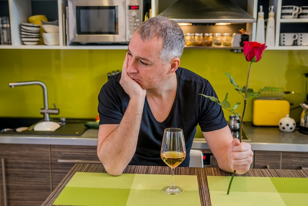 Foto homem atraente com flores em sua mão está esperando. o homem pensativo na cozinha, espera pela mulher