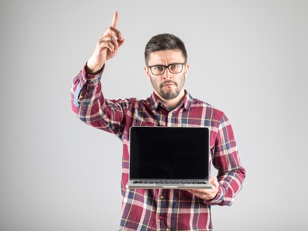 Homem atraente com laptop em branco mostrando o dedo indicador