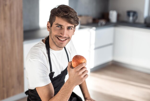 Homem atraente com uma maçã sentado em uma cozinha em casa