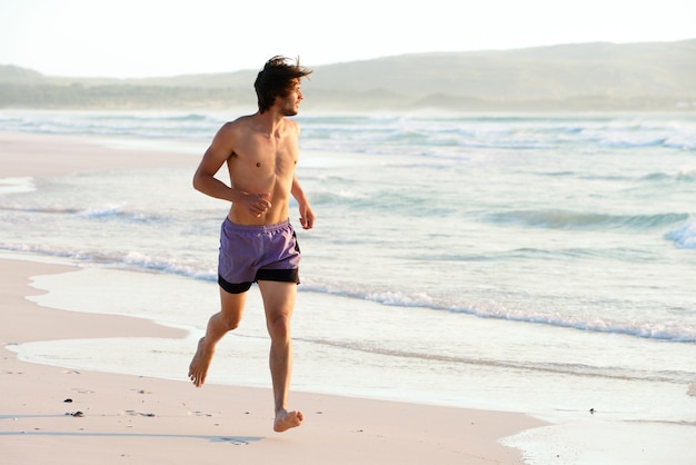 Homem atraente correndo sem camisa na praia