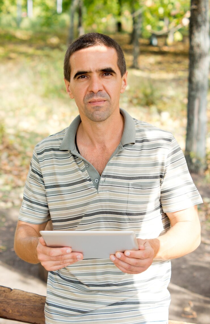 Foto homem atraente de meia idade segurando um tablet nas mãos enquanto olha para a câmera, roupas casuais no jardim