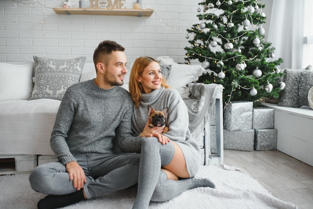 Homem atraente e alegre sentado perto da árvore de natal se abraçando