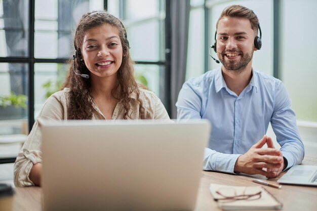 Homem atraente e mulher encantadora estão sentados em laptops em fones de ouvido