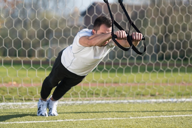 Homem atraente fazendo Crossfit com tiras Trx Fitness na área do parque da cidade treinando e exercitando para o conceito de estilo de vida saudável de resistência ao ar livre