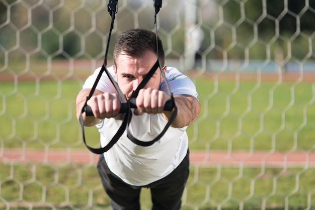 Foto homem atraente fazendo crossfit com tiras trx fitness na área do parque da cidade treinando e exercitando para o conceito de estilo de vida saudável de resistência ao ar livre