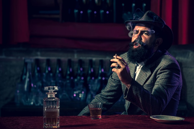 Homem atraente fumando cigarros com um copo de wiskey