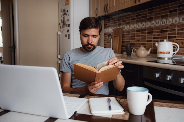 Homem atraente jovem hipster focado lendo livro no escritório em casa