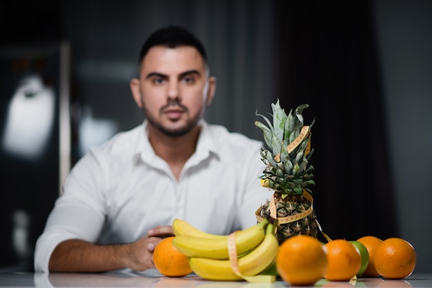 Foto homem atraente, sentado a uma mesa em que mentem frutas frescas.