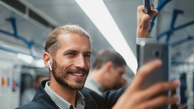 Homem atraente usando seu smartphone no trem do metrô