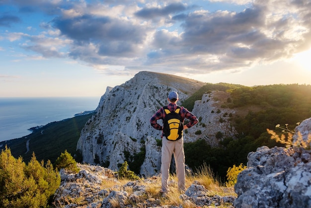 Homem aventureiro está no topo da montanha e apreciando a bela vista durante um pôr do sol vibrante