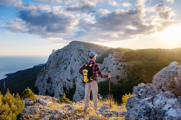 Homem aventureiro está no topo da montanha e apreciando a bela vista durante um pôr do sol vibrante