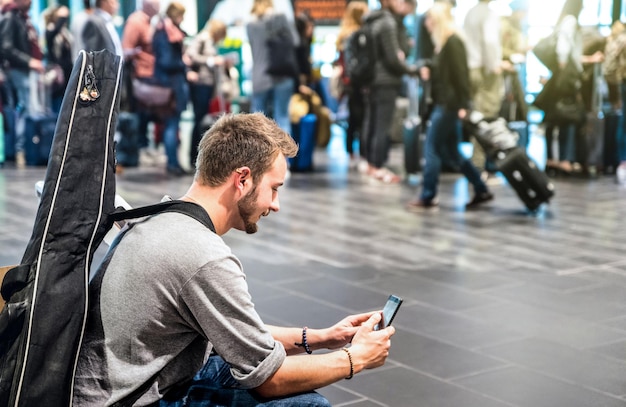 Homem aventureiro no aeroporto internacional usando telefone celular inteligente