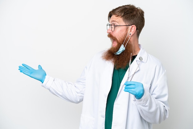 Homem avermelhado dentista segurando ferramentas isoladas em fundo branco com expressão de surpresa enquanto olha de lado