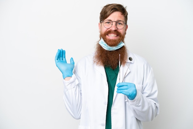 Homem avermelhado dentista segurando ferramentas isoladas em fundo branco, estendendo as mãos para o lado para convidar para vir