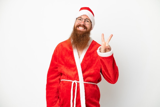 Foto homem avermelhado disfarçado de papai noel isolado no branco sorrindo e mostrando sinal de vitória