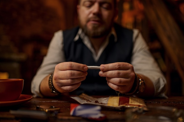 Homem babando cigarro enrolado à mão, mesa de madeira no fundo. cultura de fumar tabaco, sabor rico específico. fumante masculino lazer no escritório