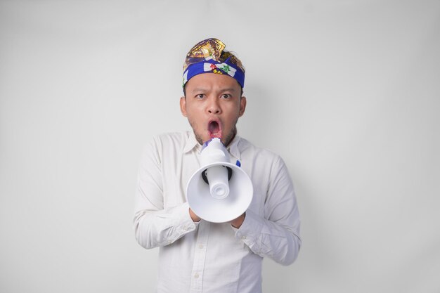 Homem balinês cheio de alegria com camisa branca e chapéu tradicional gritando em megafone sentindo-se emocionado isolado por um fundo branco