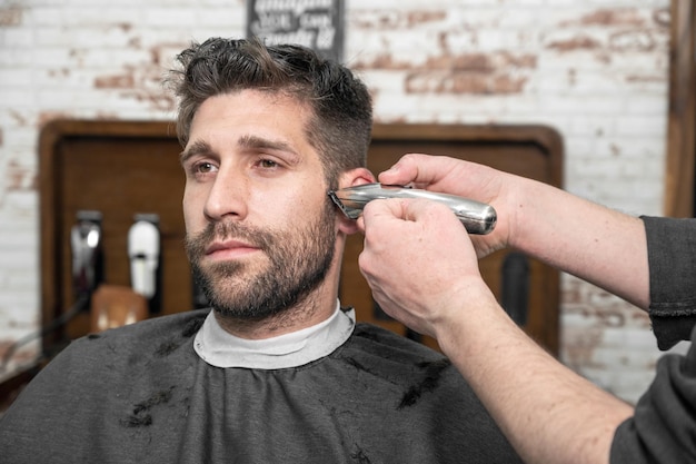 Homem barbeiro cortando o cabelo do cliente masculino com aparador na barbearia Processo de penteado Fotografia de alta qualidade