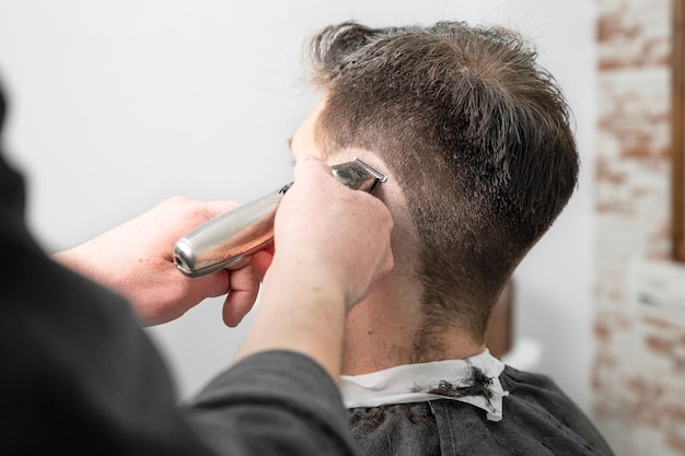 Homem barbeiro cortando o cabelo do cliente masculino com aparador na barbearia Processo de penteado Fotografia de alta qualidade