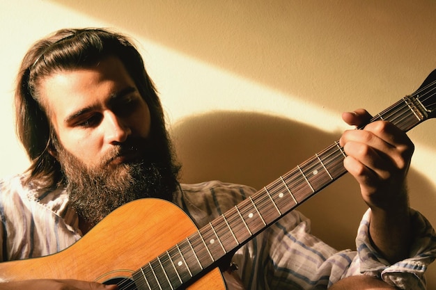 Homem barbudo a tocar guitarra contra a parede em casa