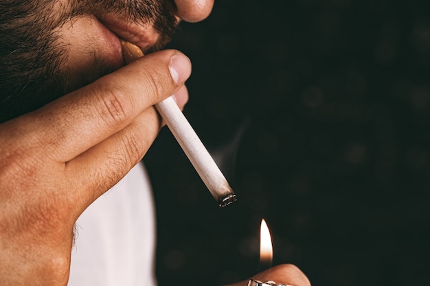 Foto homem barbudo acendendo cigarro com o isqueiro close-up