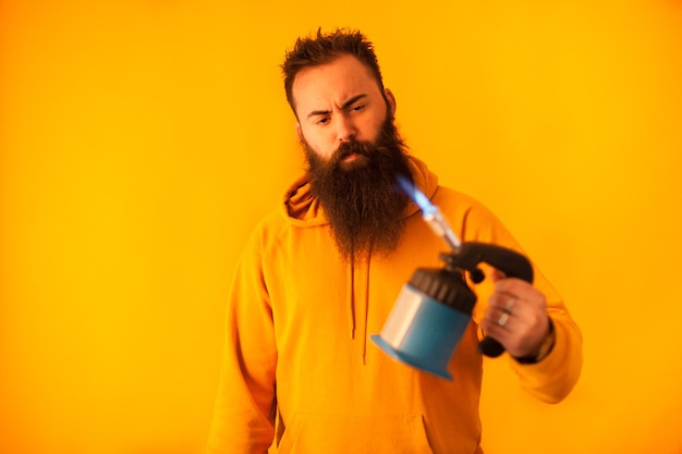 Homem barbudo acessível segurando maçarico sobre fundo amarelo. ferramenta profissional. ferramenta azul