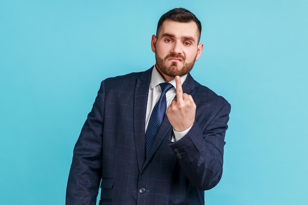 Foto homem barbudo agressivo descortês vestindo terno estilo oficial mostrando o dedo médio e pedindo para sair expressando negatividade comportamento desrespeitoso tiro de estúdio interior isolado em fundo azul