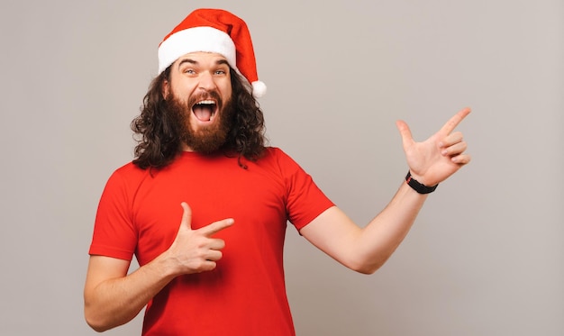 Homem barbudo animado está apontando com as duas mãos de lado na oferta de Natal