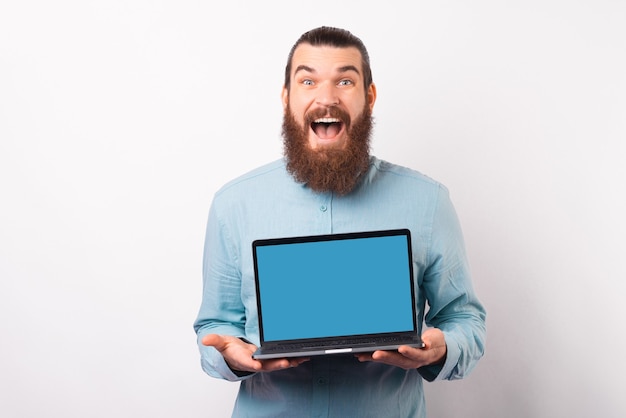 Homem barbudo animado está mostrando para a câmera a tela do laptop.