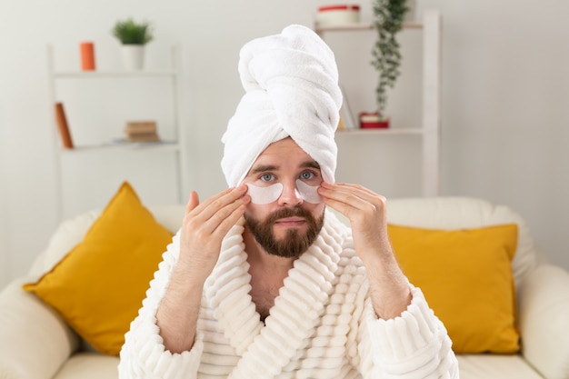 Homem barbudo aplicando tapa-olhos no rosto. rugas e cuidados domiciliares de rosto para homens.