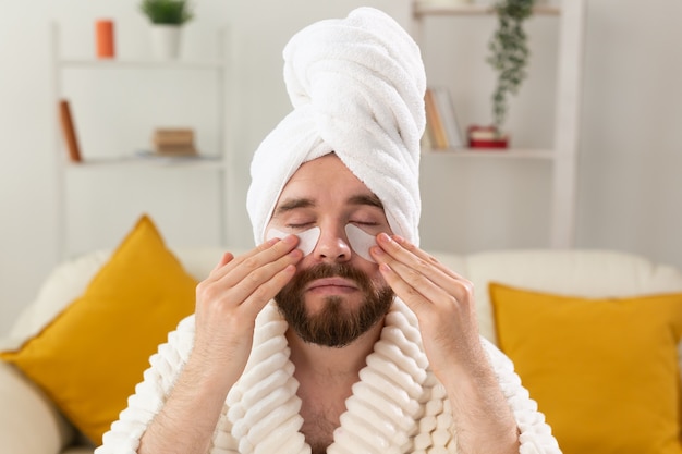 Homem barbudo aplicando tapa-olhos no rosto. rugas e cuidados domiciliares de rosto para homens.