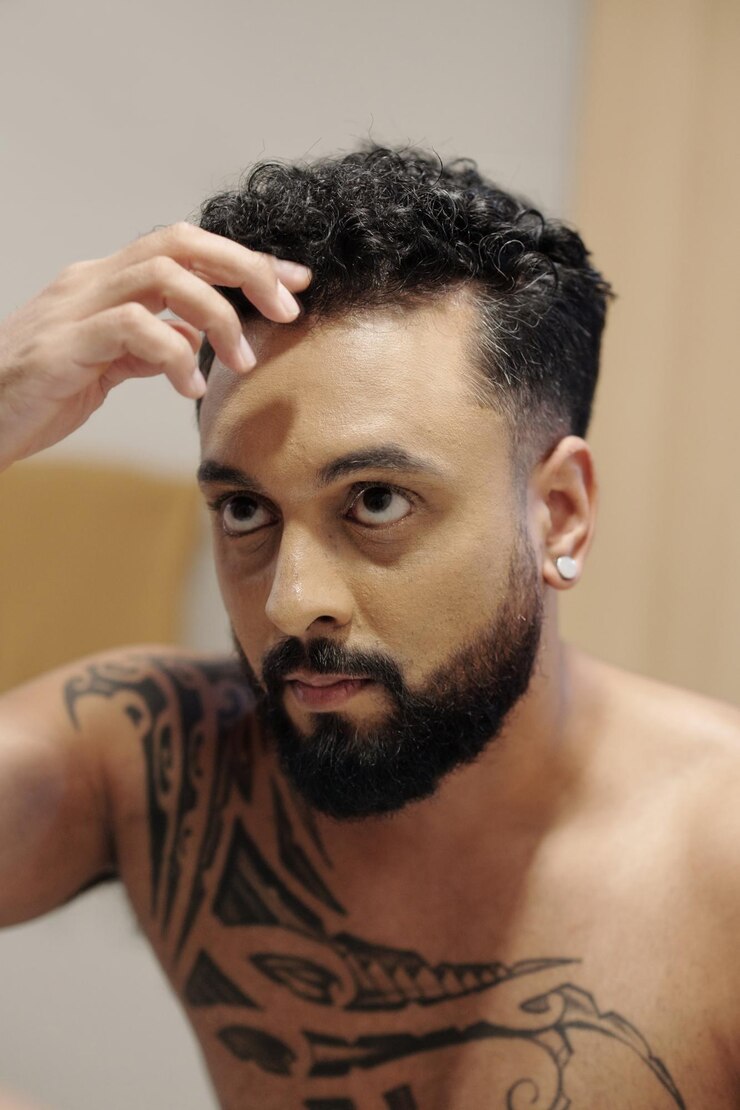 Foto homem barbudo atraente ajeitando o cabelo em frente ao espelho do banheiro quando se arruma pela manhã
