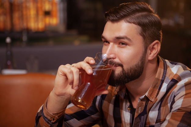 Homem barbudo atraente, desfrutando de copo de cerveja no pub