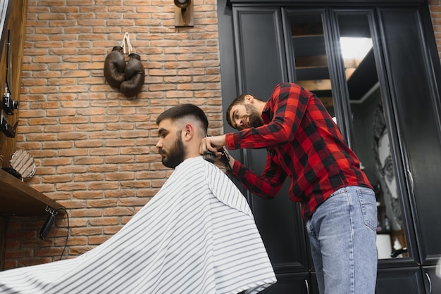 Homem barbudo bonito sorrindo enquanto tem seu cabelo cortado por cabeleireiro na barbearia